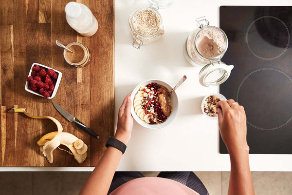 An overhead shot of a woman preparing a healthy pre-workout breakfast containing oats, fruit, nut butter, and protein powder
