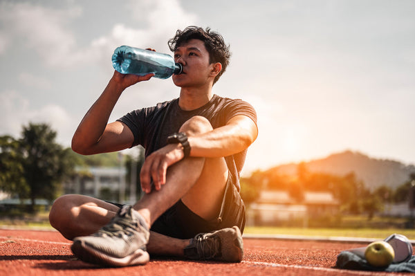 Young man rehydrating on a running track.