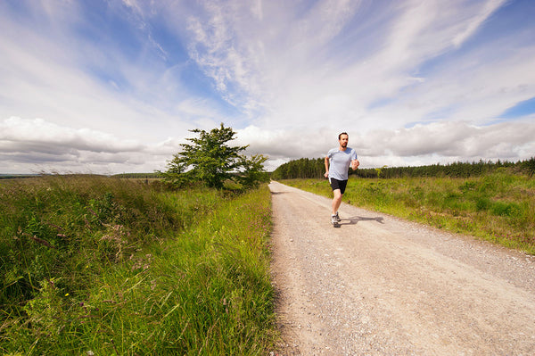 A man goes for a run on a dirt road through a field