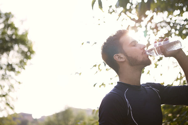 A young man drinks a bottle of water while exercising.