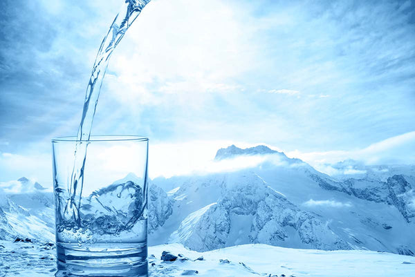 A clear glass of refreshing water in the foreground of a snowy, icy mountain glacier